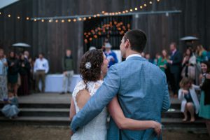 The barn at Cuffey's Cove is lit up with Christmas lights, inside and out. The bride and groom stand outside laughing with their arms around each other.