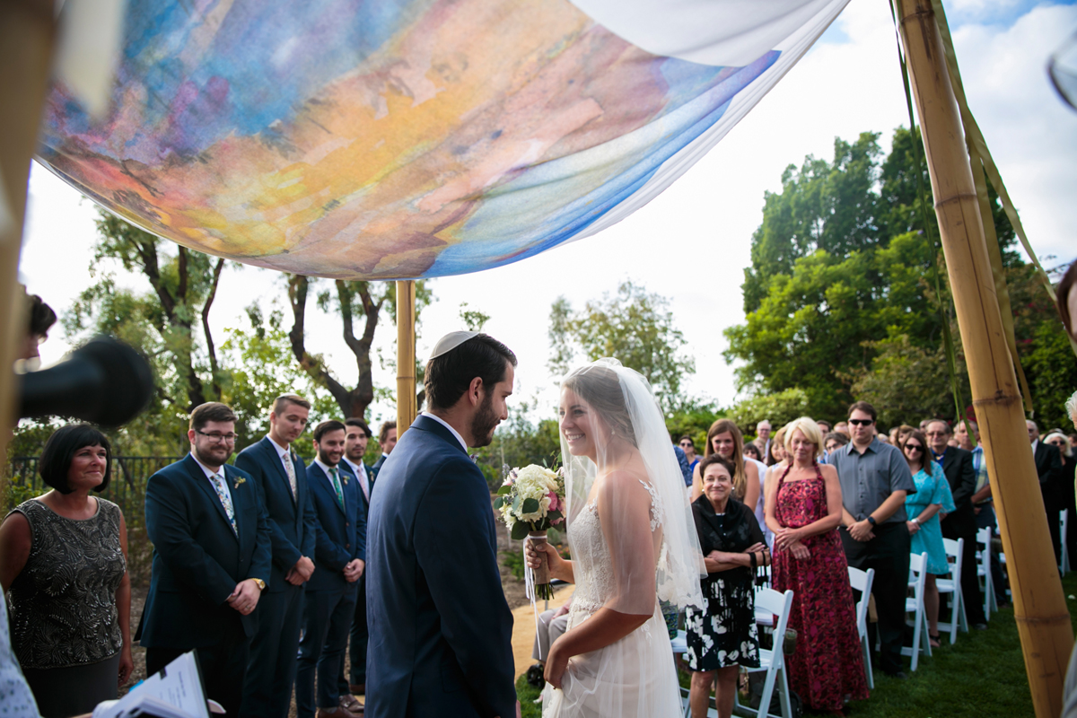 Bride circles the groom under a colorful watercolor painting chuppah.