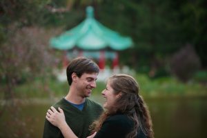 The engaged couple are laughing with each other in front of the Chinese Pavilion at Stow Lake.