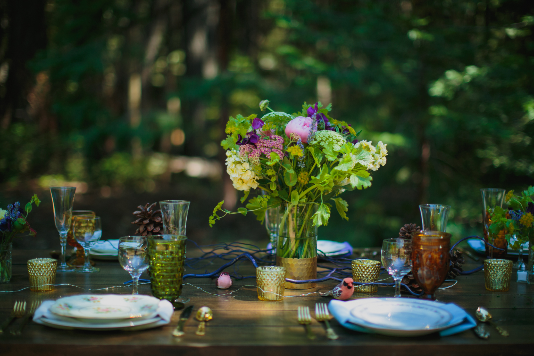 The table scape of flowers, mismatched glassware, vintage plates and pinecones.