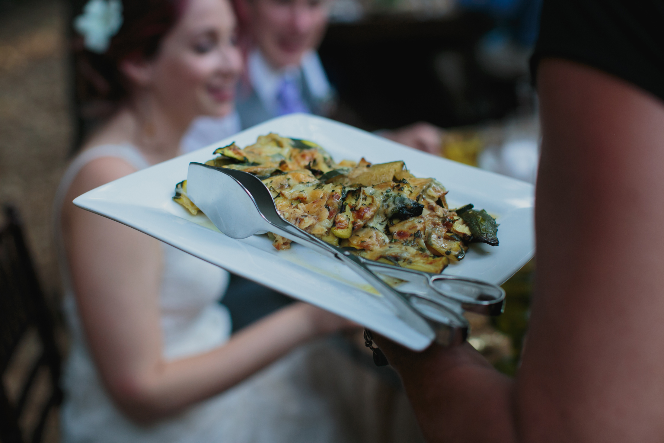 A plate of food is being served with a smiling bride in the background.