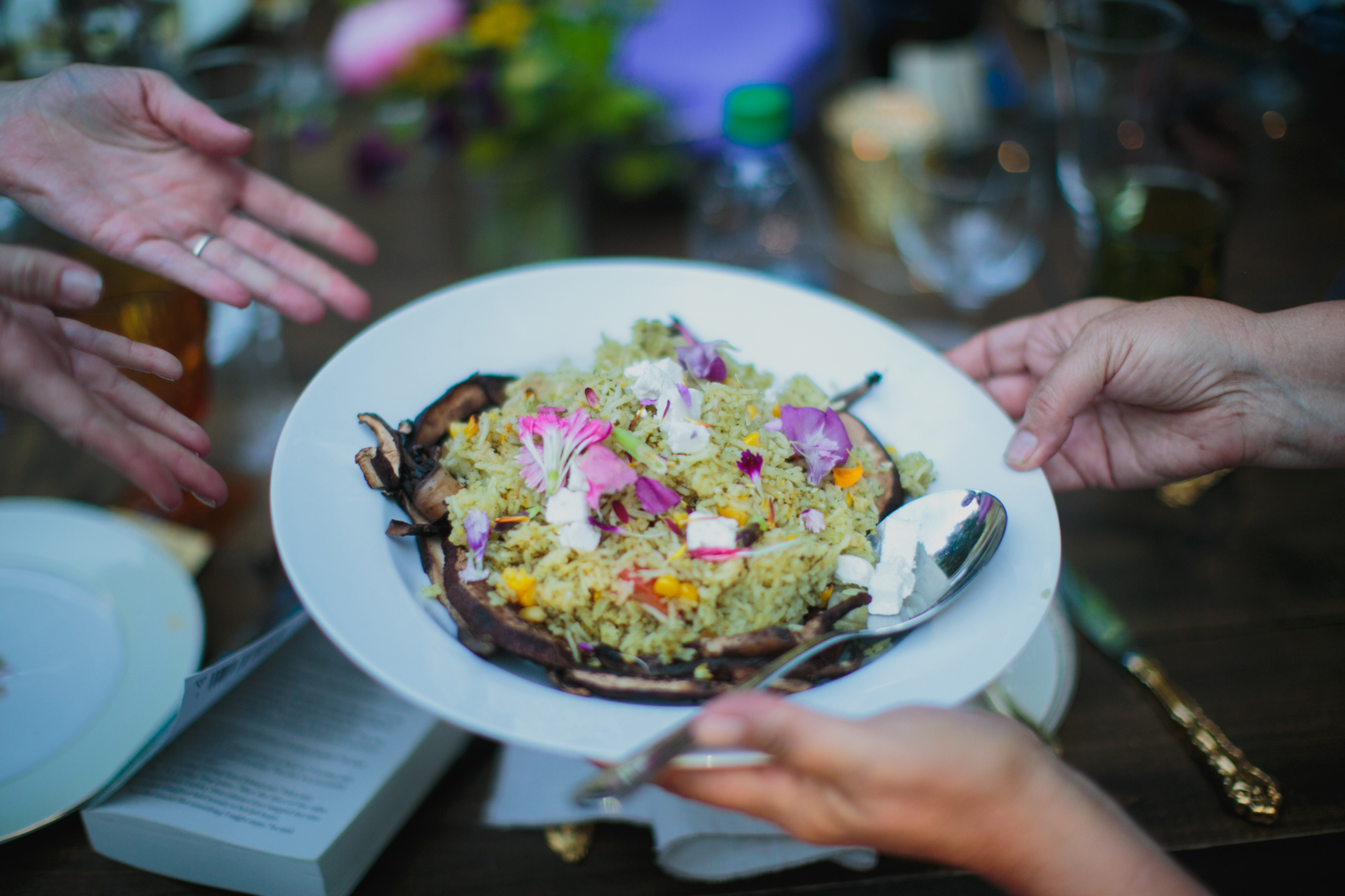 A plate of risotto and flower garnishes is being passed around at the family-style dinner.
