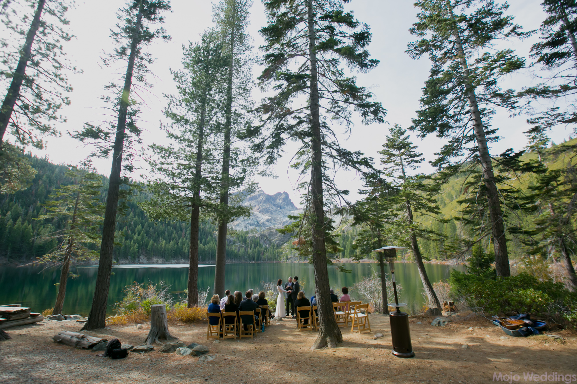 A very wide look at the entire ceremony showing all the guests, trees, and mountains surrounding them.