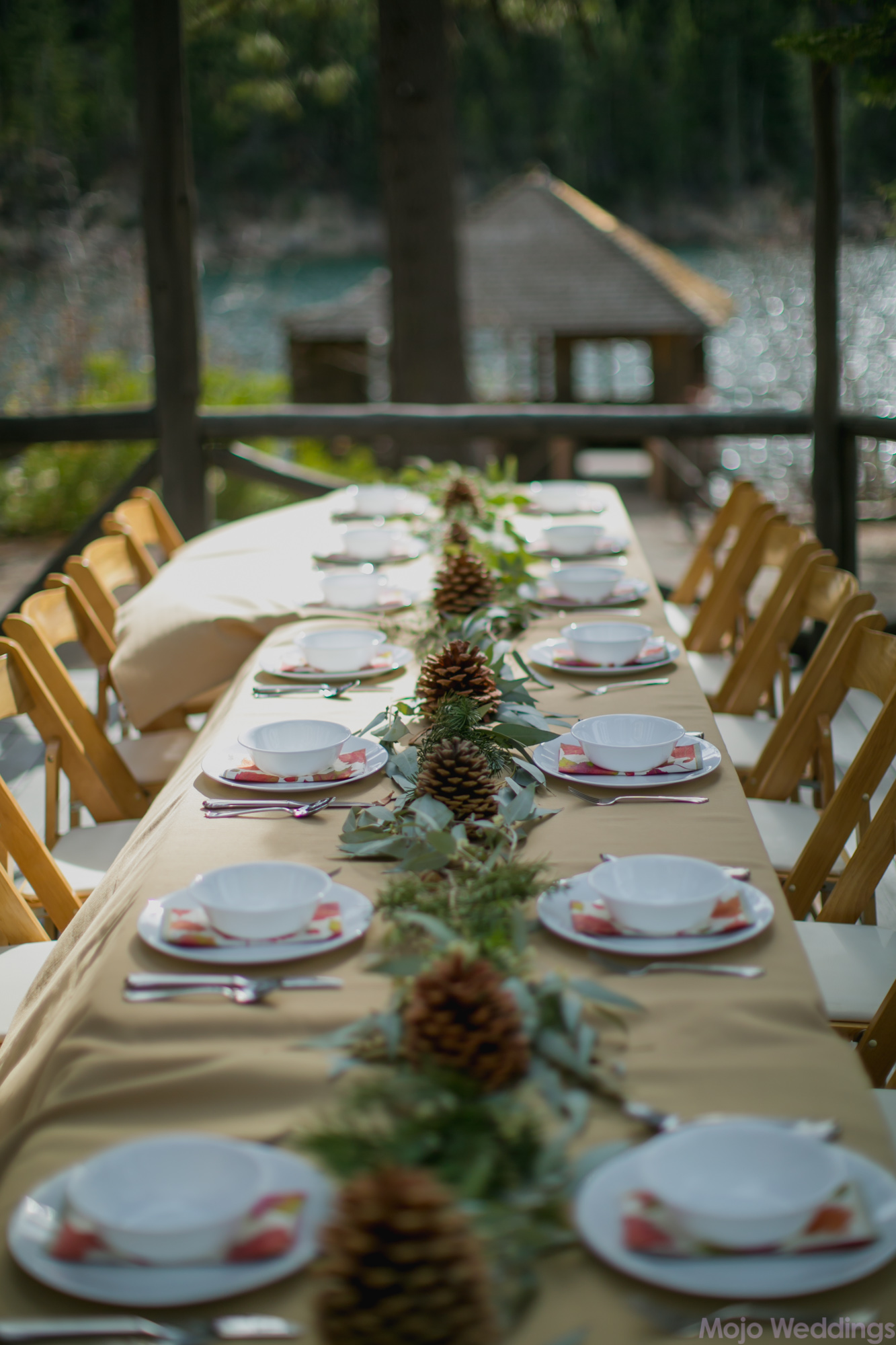 The table scape shows white bowls, napkins with fall colored leaves, and pine cone centerpieces.