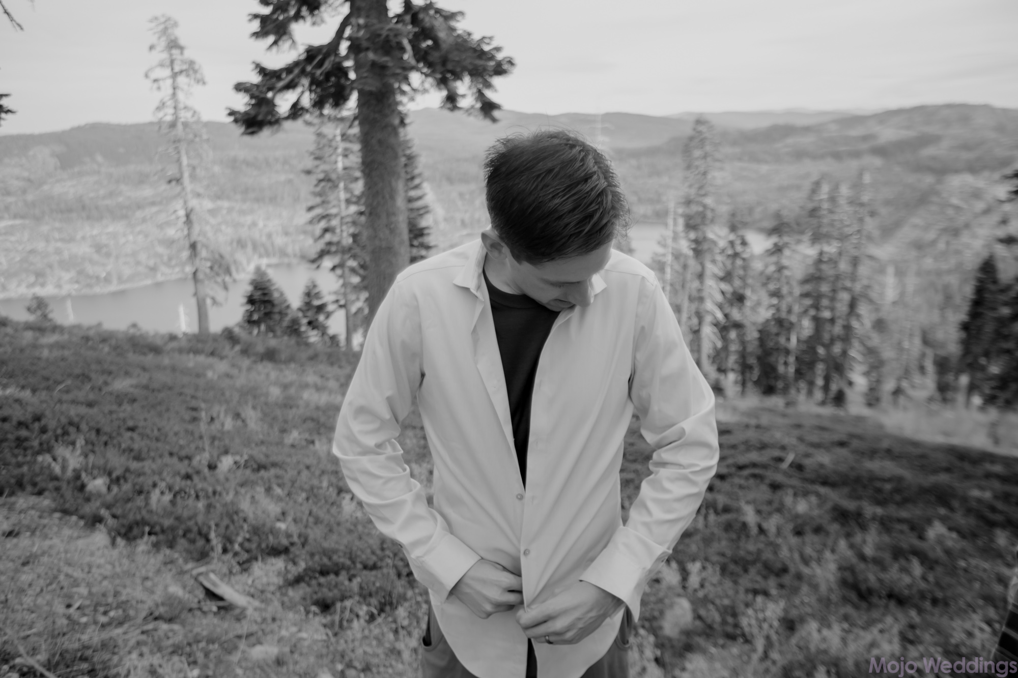 A black and white of the groom getting ready in the mountains.