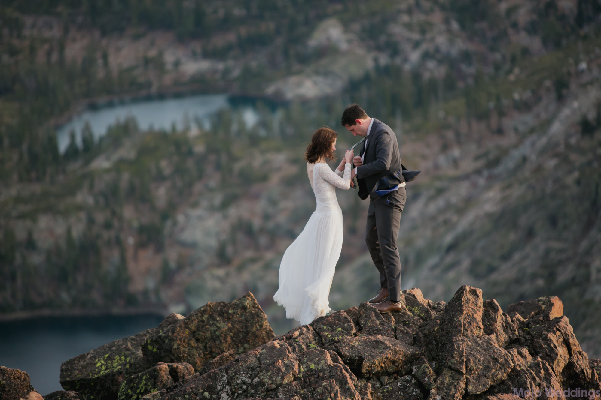 She fixes his tie as they carefully stand on the mountaintop.